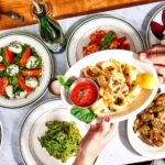Group with spaghetti, caprese, one guest hands a plate of food to another