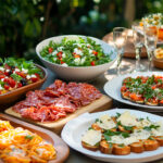 Wooden platters outdoors with salami, spaghetti, salads, and champagne glasses