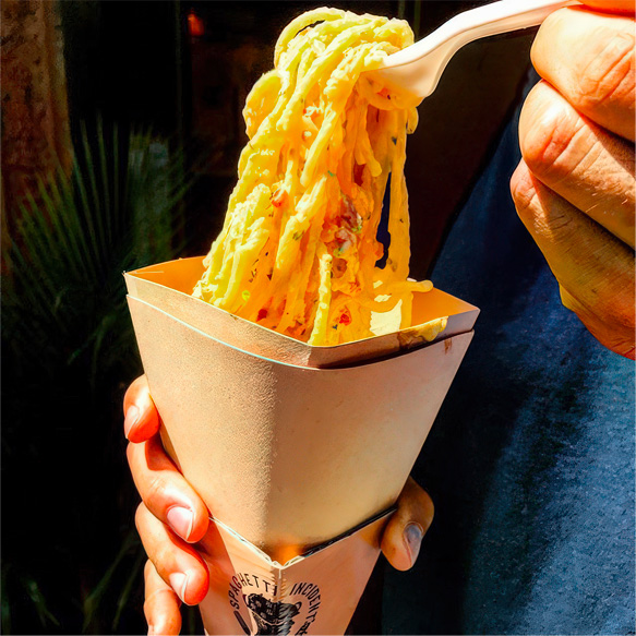 Man lifting some carbonara spaghetti out of a cone with a disposable fork