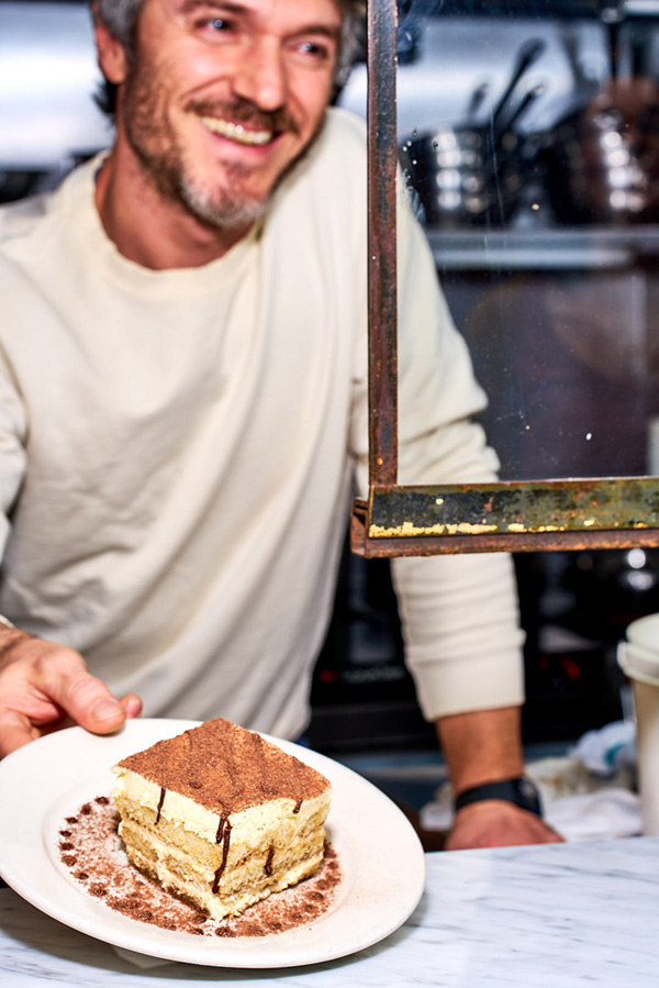 Giovanni Gentile smiling while serving tiramisu on a plate